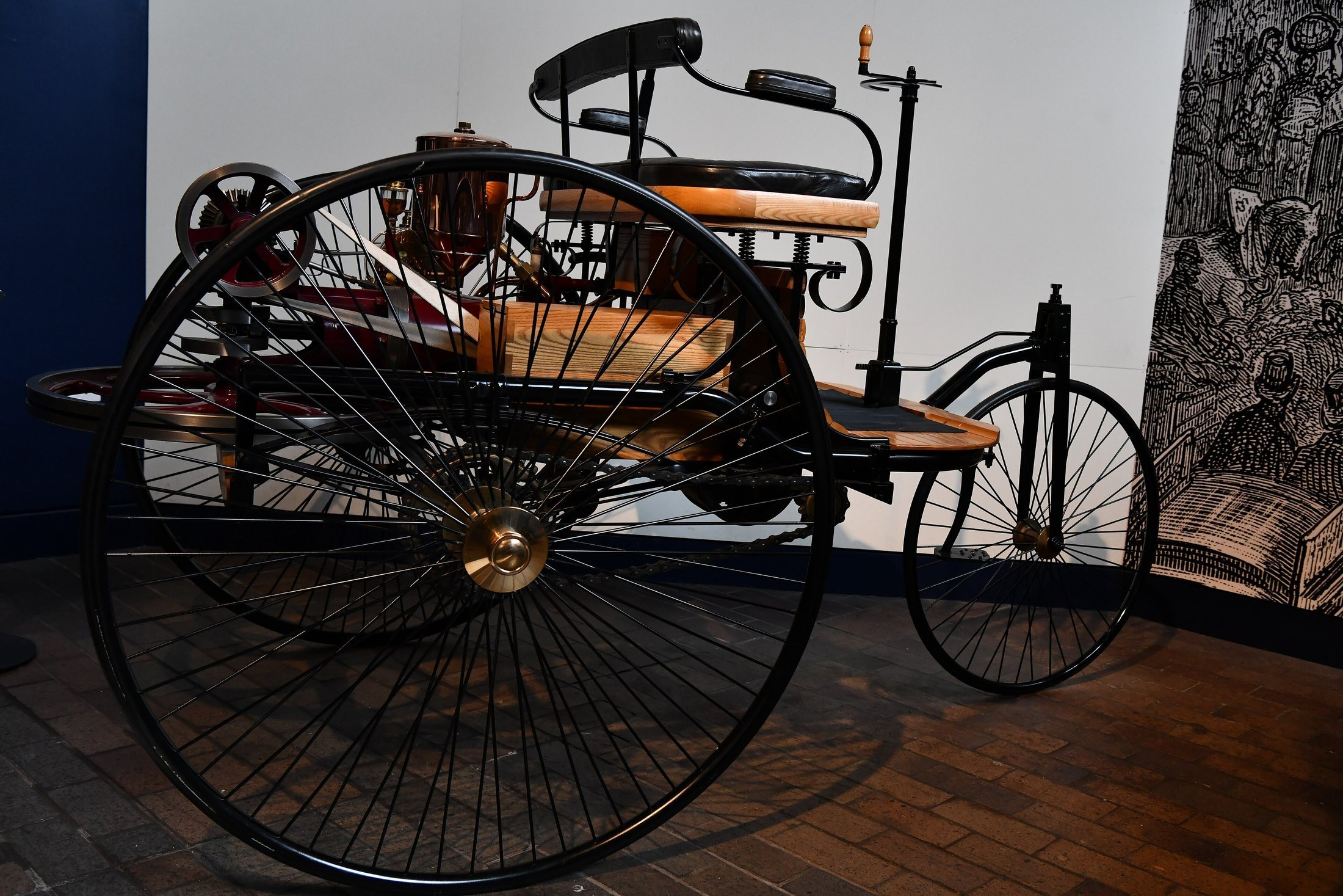 An early Benz car in a museum with large thin wheels and an open seat.