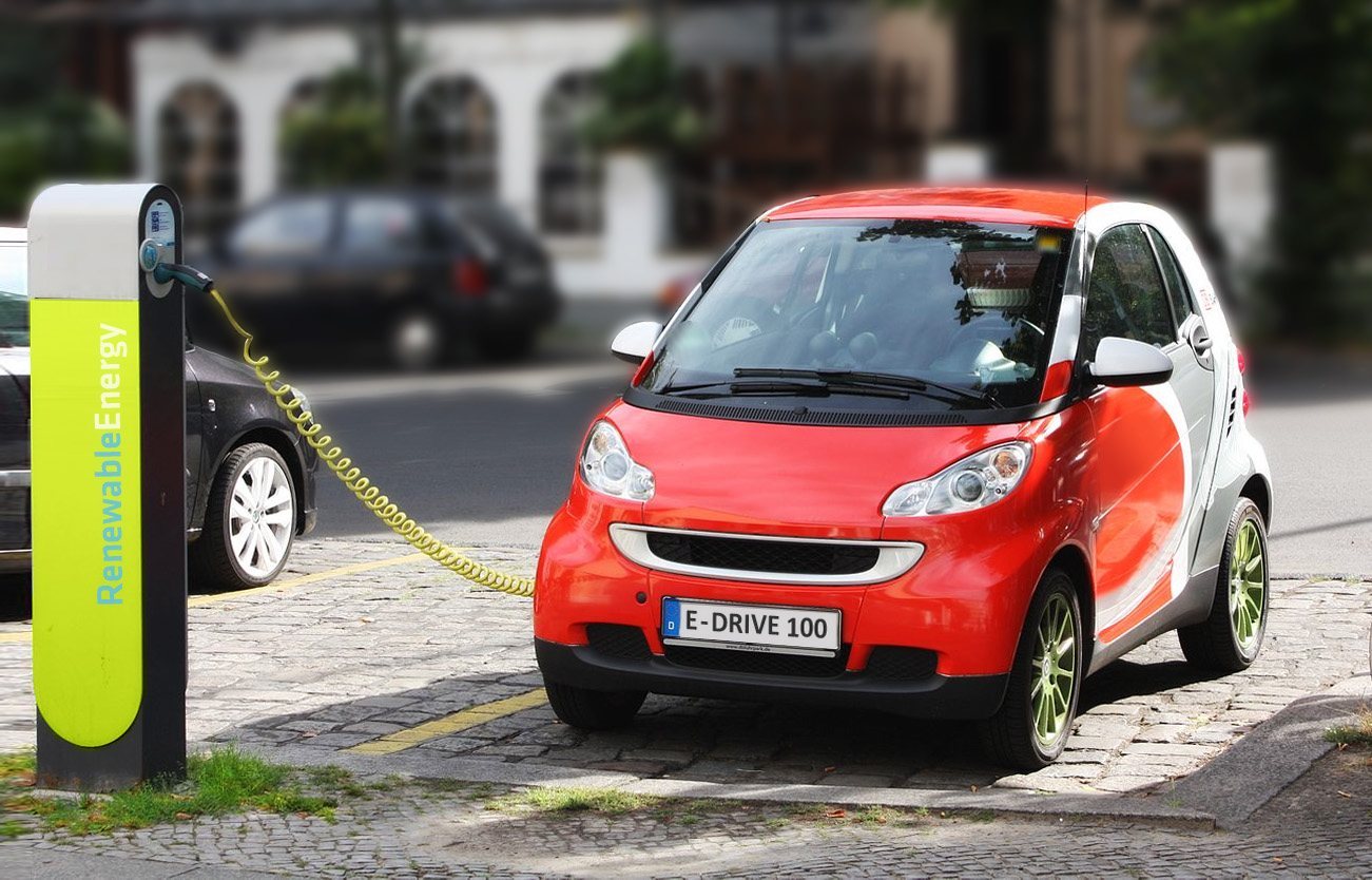 A small electric car parked while recharging at a charging station.