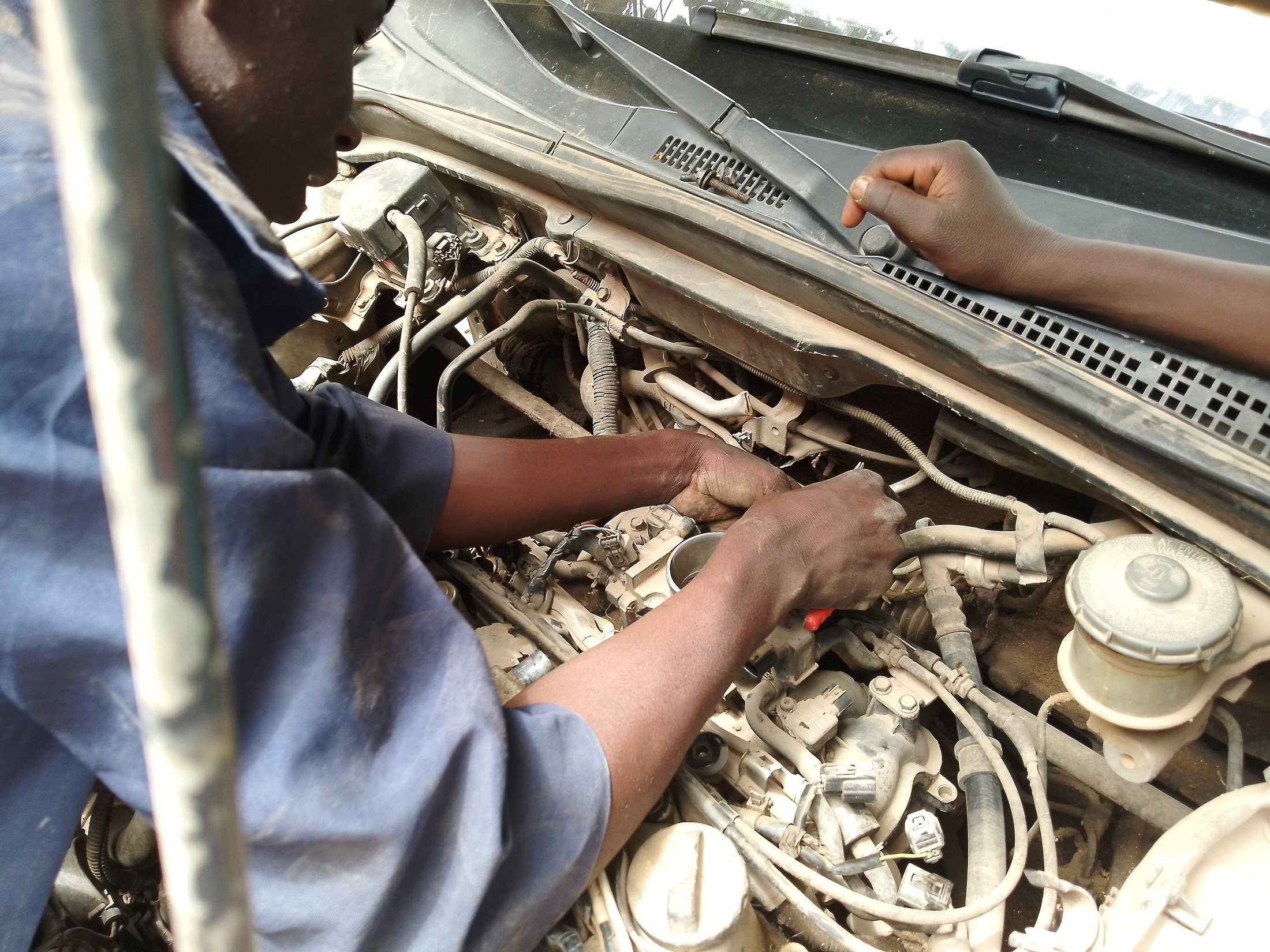 A mechanic looking under a car hood and repairing the engine.