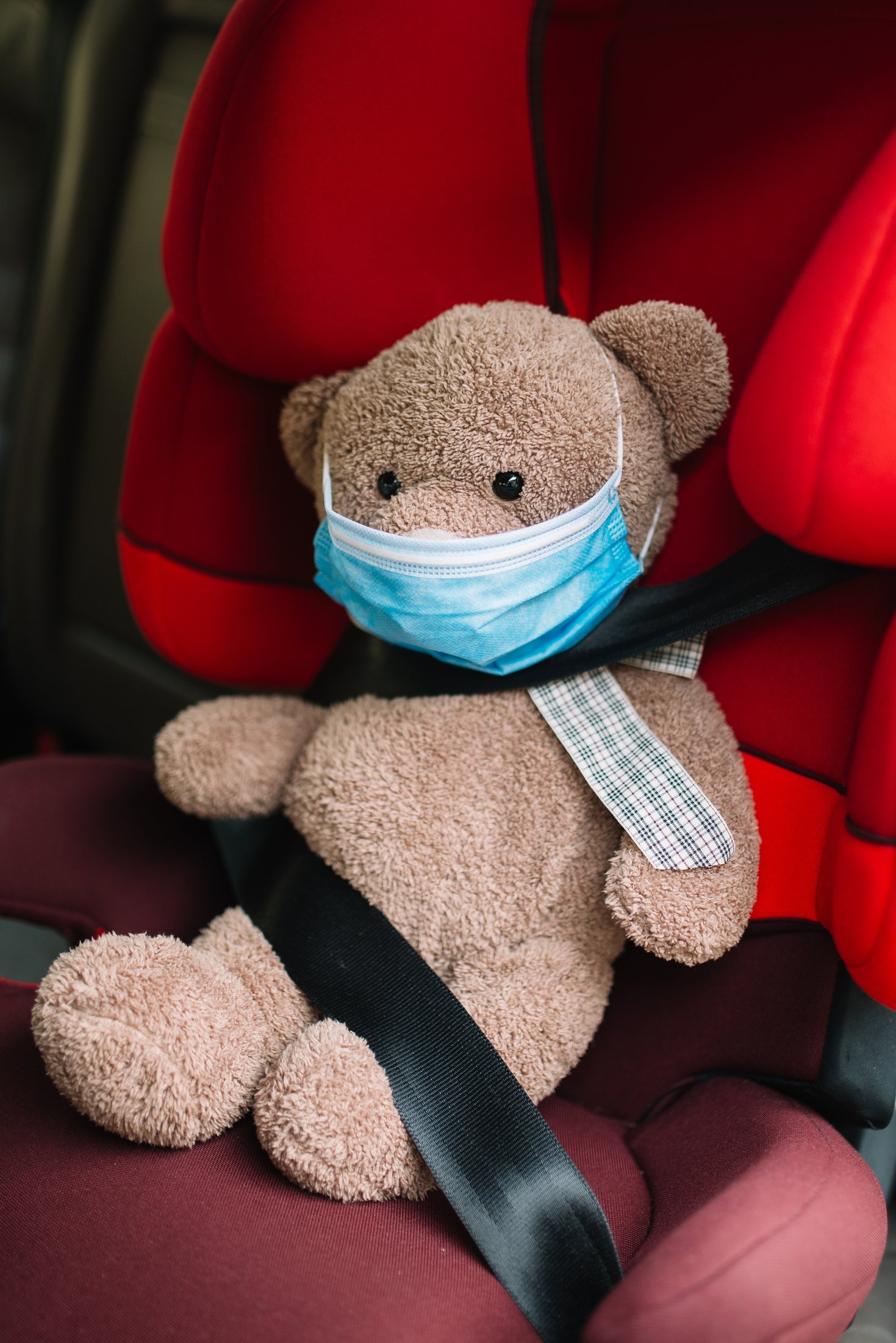 A teddy bear toy buckled into a child car seat.