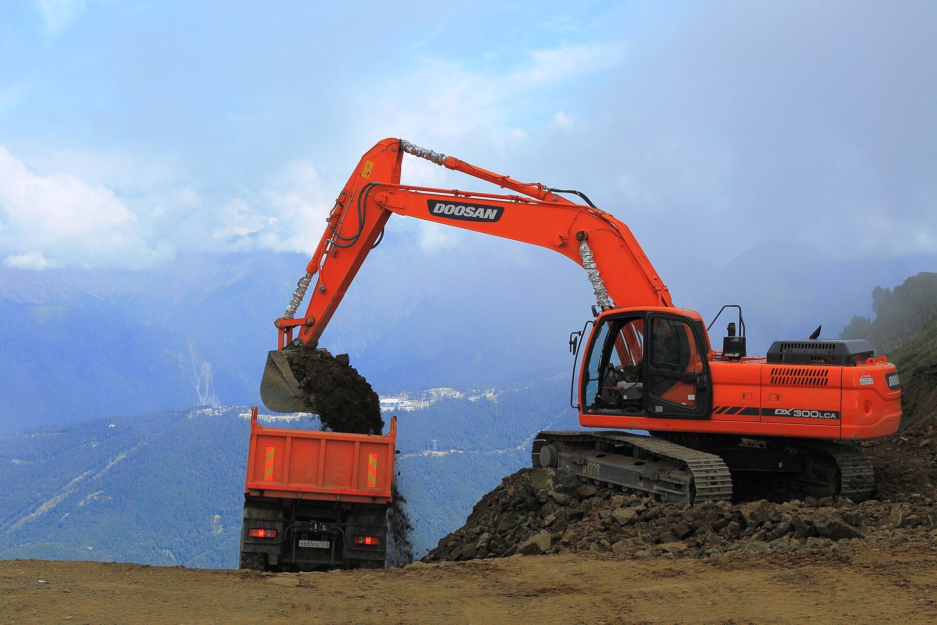 An excavator loading dirt into a dump truck while building a road on a mountain ridge