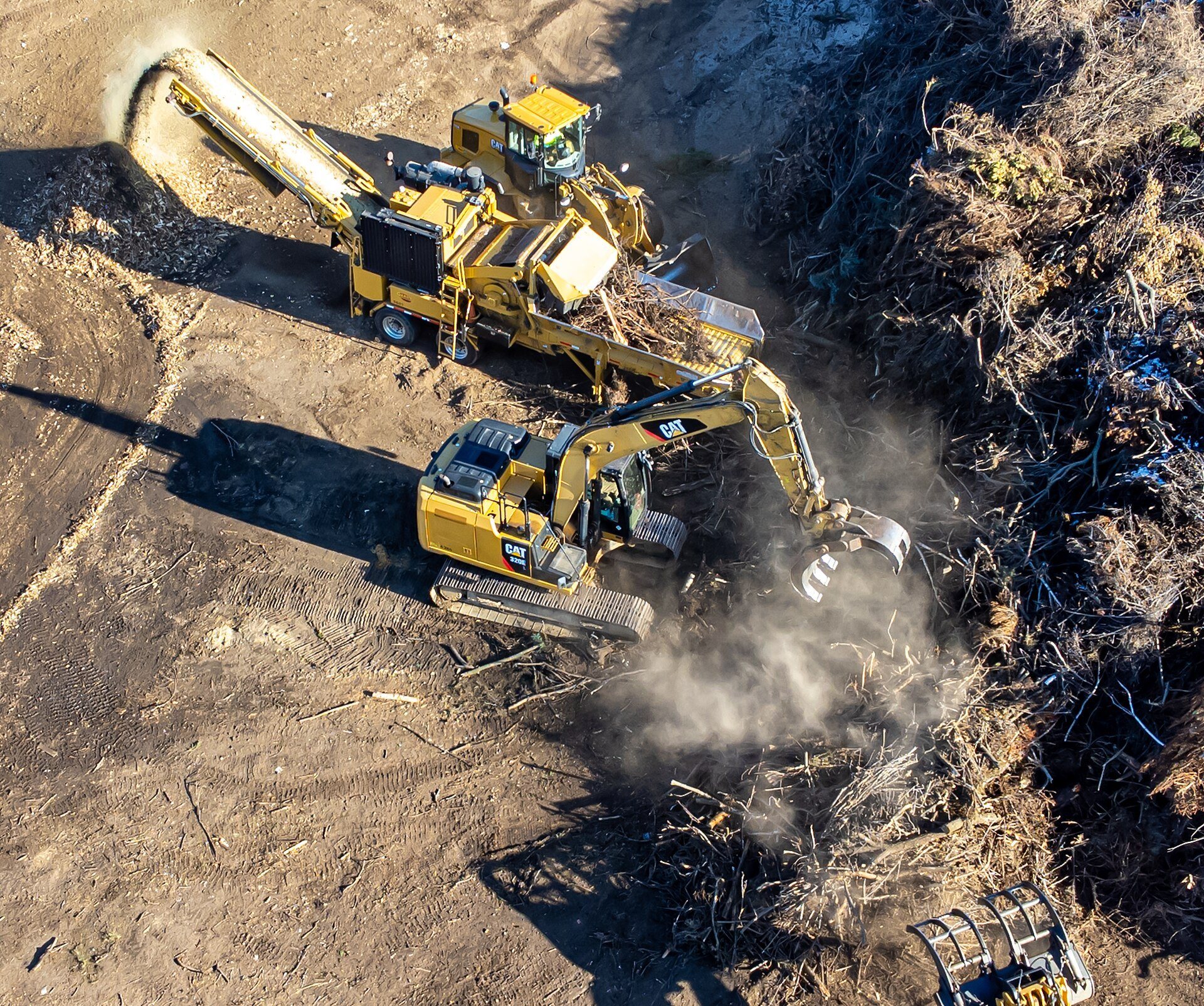 An excavator using a grapple attachment to pick up material and feed it into a chipper
