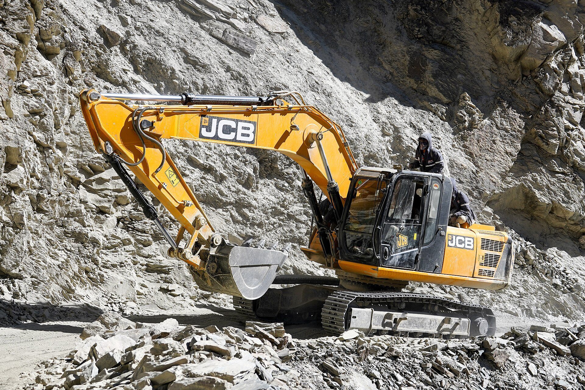 A JCB excavator carving a road through steep mountains in India