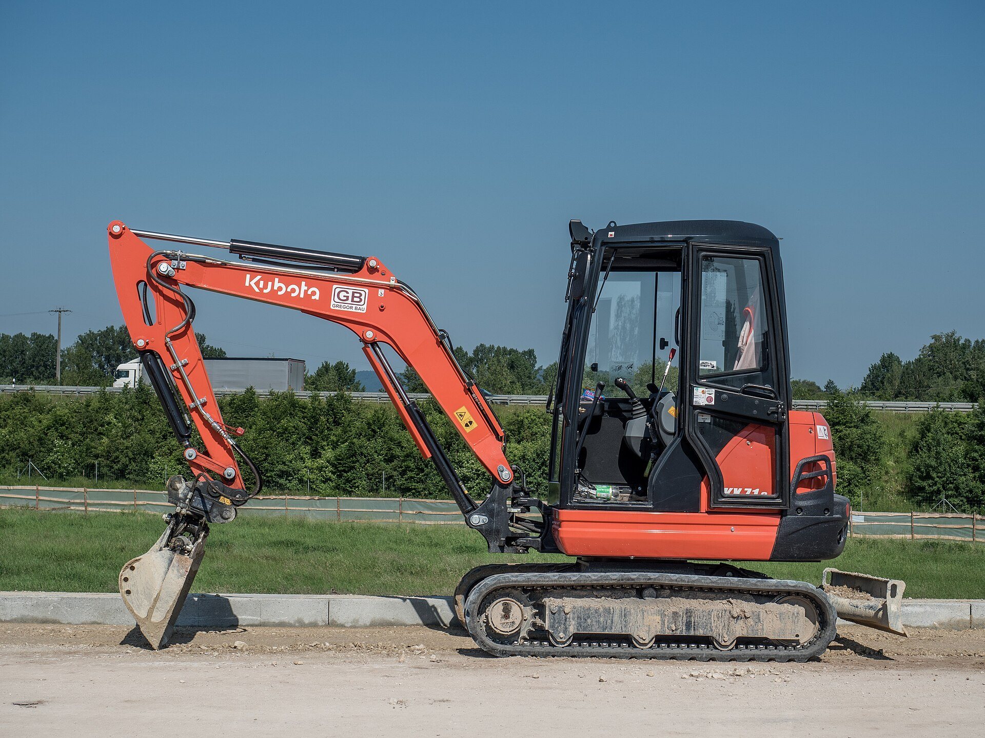 A small orange Kubota excavator clearly showing its tracks, cab, boom, arm, and bucket