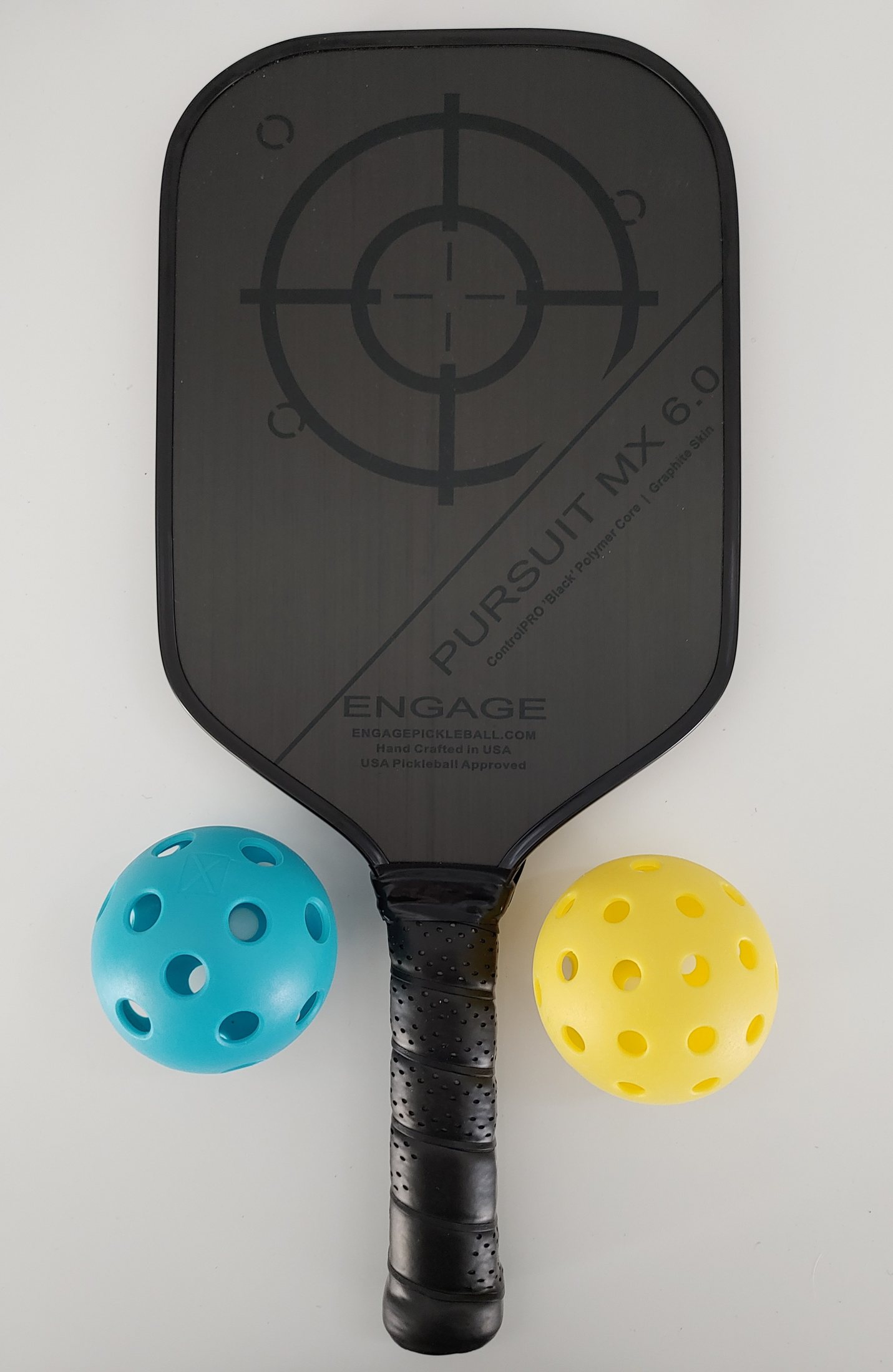 A pickleball paddle next to a blue indoor ball and a yellow outdoor ball, showing the difference in hole size between the two types
