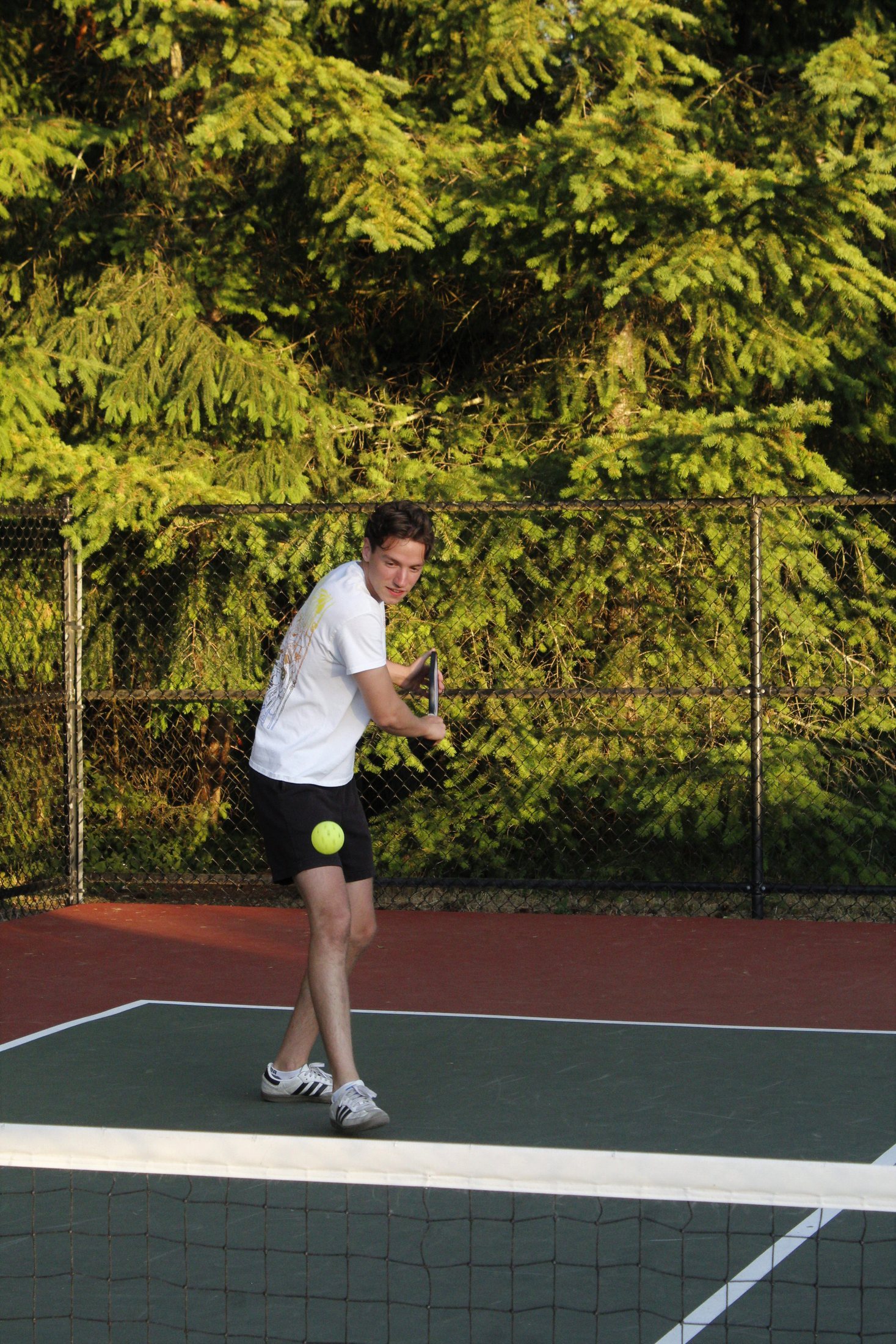 A pickleball player crouched low, preparing to return the ball with a backhand stroke on an outdoor court