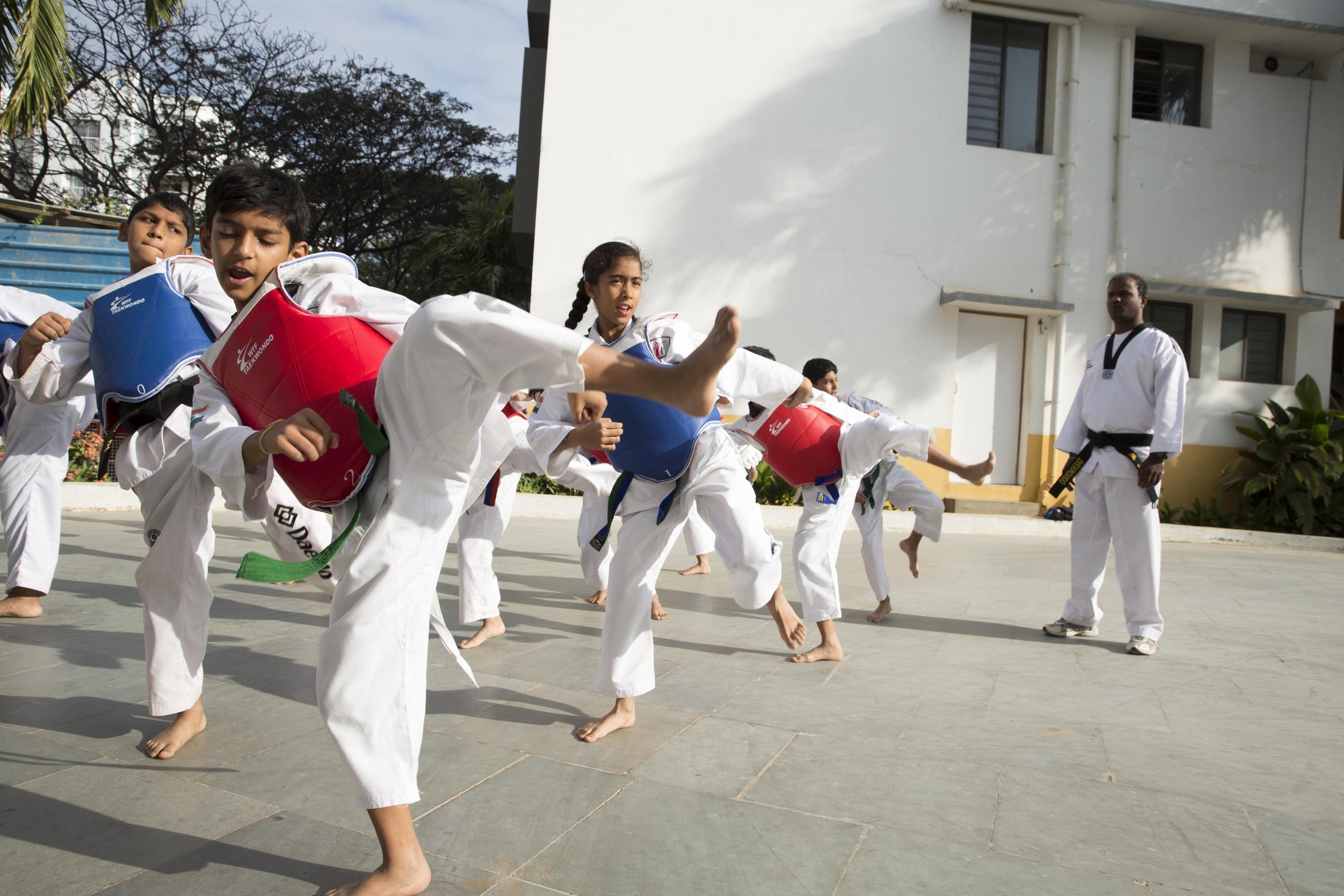 A group of schoolchildren in taekwondo uniforms and colored belts practicing together.