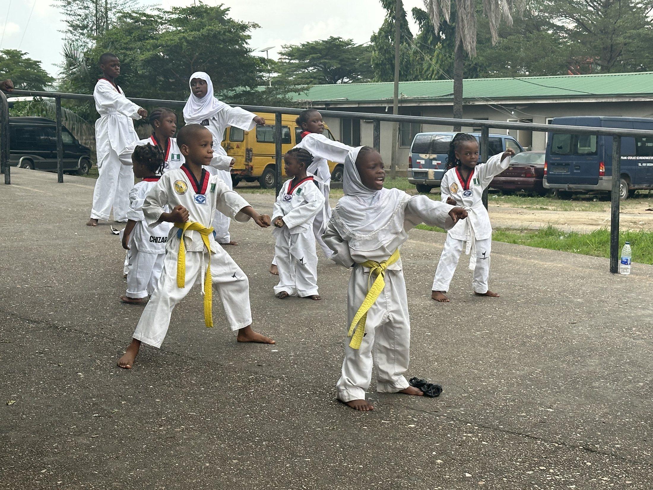 Children in white taekwondo uniforms practicing together outside at National Stadium.