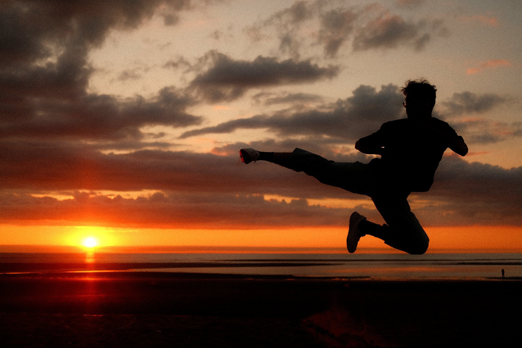 A taekwondo athlete performing a dramatic jumping side kick against a sunset sky.